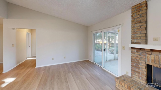 unfurnished room with a fireplace, vaulted ceiling, light hardwood / wood-style flooring, and a textured ceiling