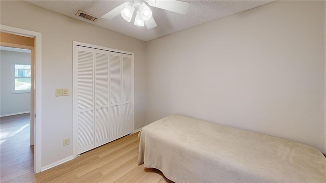 bedroom featuring ceiling fan, a closet, a textured ceiling, and light wood-type flooring