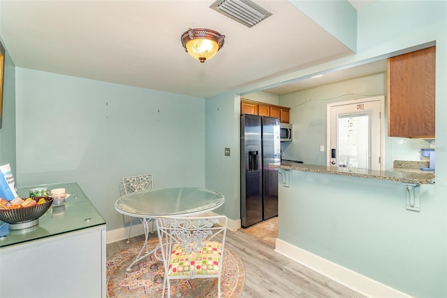 kitchen featuring kitchen peninsula, light stone counters, light hardwood / wood-style floors, and appliances with stainless steel finishes