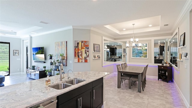 kitchen with light stone counters, a raised ceiling, sink, pendant lighting, and an inviting chandelier