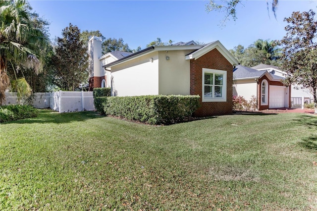 view of side of property featuring a garage, brick siding, a lawn, fence, and stucco siding