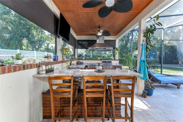 view of patio / terrace featuring a lanai, area for grilling, fence, a ceiling fan, and an outdoor bar