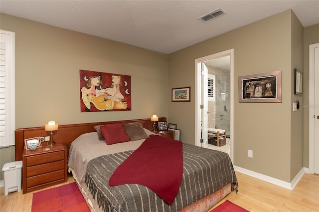 bedroom with visible vents, a textured ceiling, baseboards, and wood finished floors