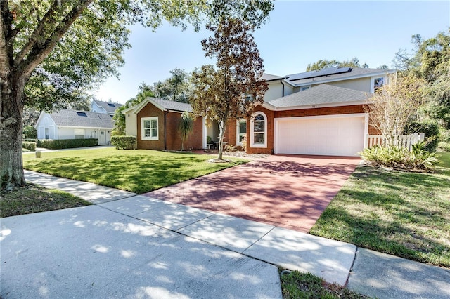 view of front of property with an attached garage, brick siding, decorative driveway, roof mounted solar panels, and a front lawn