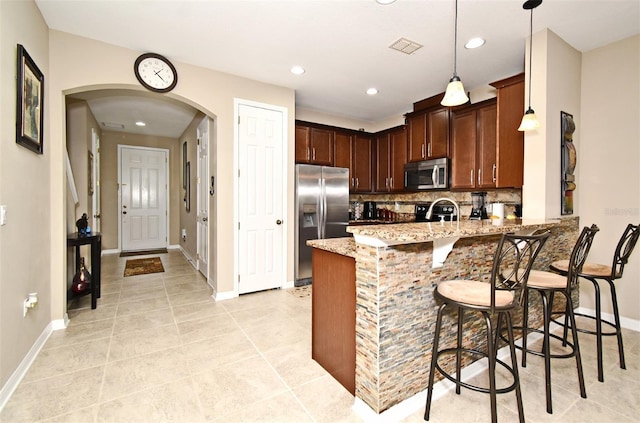 kitchen with a breakfast bar area, stainless steel appliances, kitchen peninsula, pendant lighting, and light stone counters