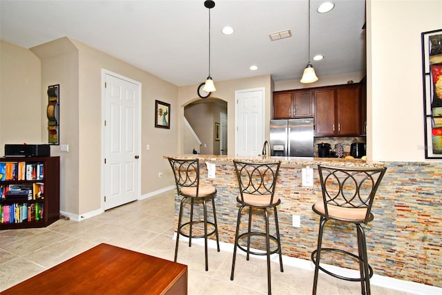 kitchen featuring a kitchen breakfast bar, light stone countertops, light tile patterned floors, pendant lighting, and stainless steel refrigerator with ice dispenser