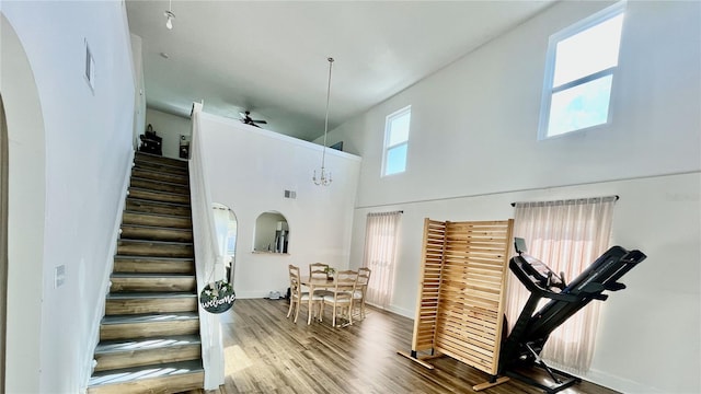 interior space featuring ceiling fan with notable chandelier, wood-type flooring, and a high ceiling