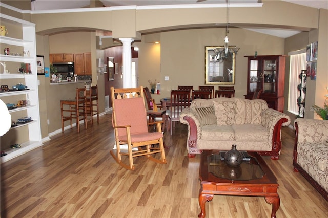 living room featuring a chandelier, vaulted ceiling, decorative columns, and light hardwood / wood-style flooring