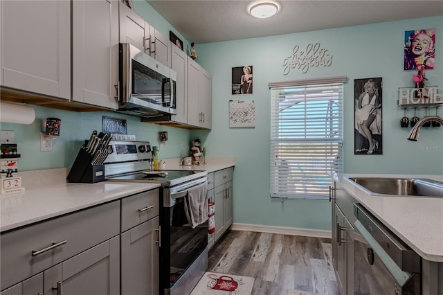 kitchen featuring sink, light hardwood / wood-style flooring, gray cabinets, a textured ceiling, and appliances with stainless steel finishes