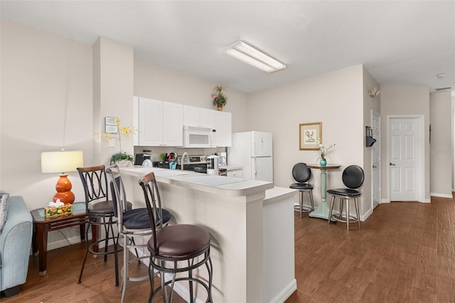 kitchen with a breakfast bar, white appliances, white cabinets, dark hardwood / wood-style flooring, and kitchen peninsula