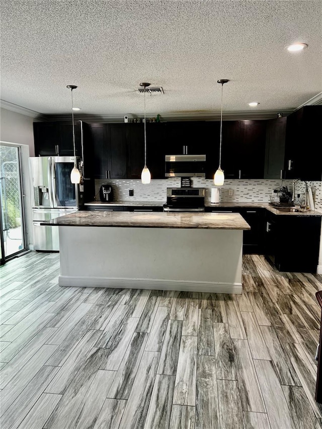 kitchen featuring decorative light fixtures, a center island, range hood, and appliances with stainless steel finishes