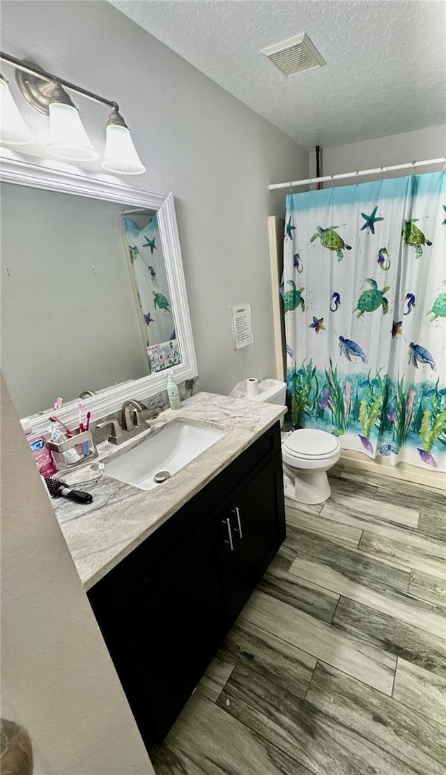 full bathroom with vanity, a textured ceiling, shower / tub combo with curtain, hardwood / wood-style floors, and toilet