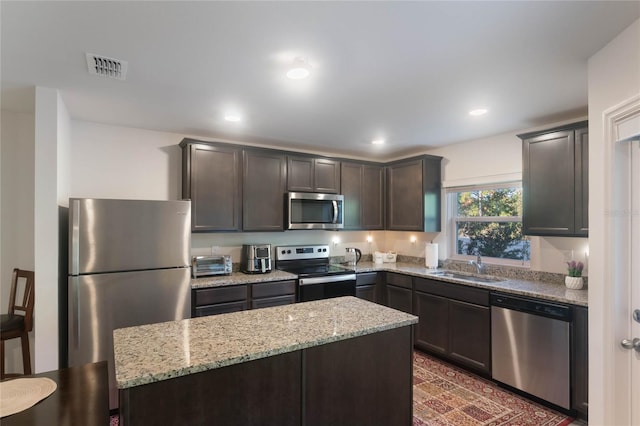 kitchen with light stone countertops, stainless steel appliances, a kitchen island, and sink