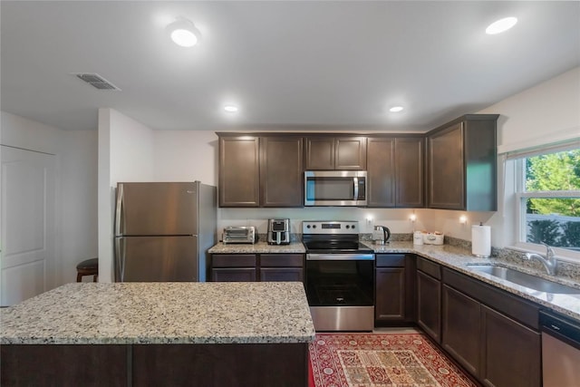 kitchen with light stone countertops, sink, a center island, and appliances with stainless steel finishes