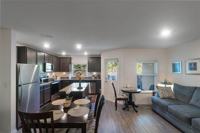 kitchen featuring hardwood / wood-style floors, a center island, appliances with stainless steel finishes, dark brown cabinets, and light stone counters