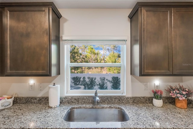 kitchen featuring light stone countertops, dark brown cabinets, and sink