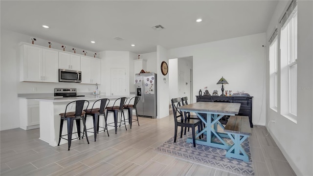 kitchen with stainless steel appliances, a center island with sink, a kitchen bar, plenty of natural light, and white cabinets