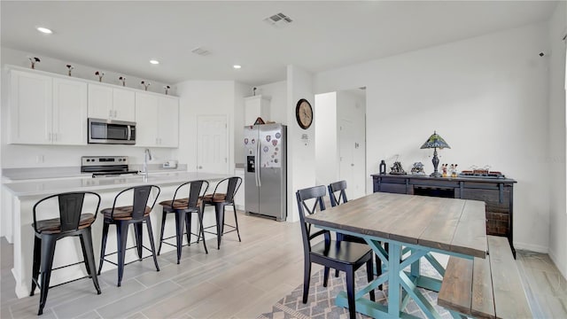 kitchen featuring appliances with stainless steel finishes, a kitchen breakfast bar, white cabinets, and a center island with sink