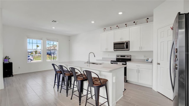 kitchen featuring a center island with sink, stainless steel appliances, a kitchen bar, sink, and white cabinetry