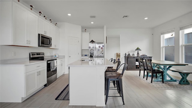 kitchen featuring stainless steel appliances, sink, white cabinets, a breakfast bar area, and a center island with sink