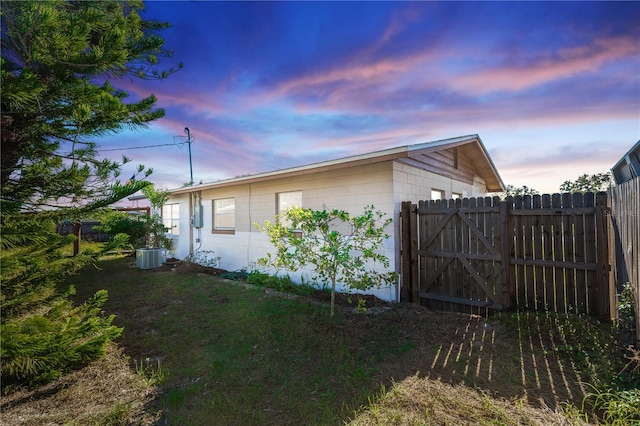 property exterior at dusk with central air condition unit and a lawn