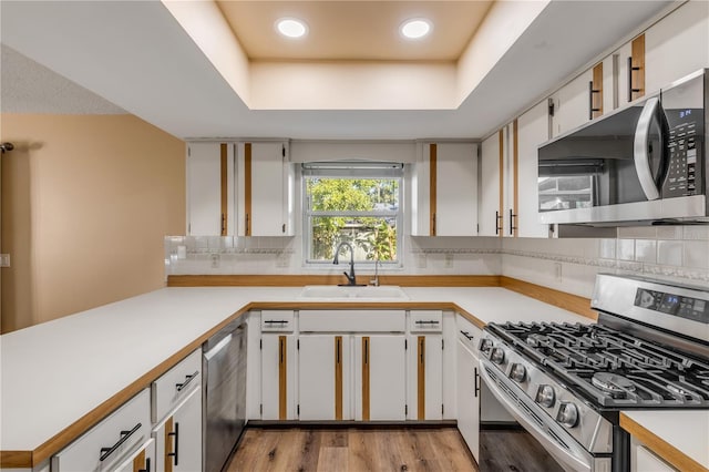 kitchen with white cabinets, sink, appliances with stainless steel finishes, tasteful backsplash, and light hardwood / wood-style floors