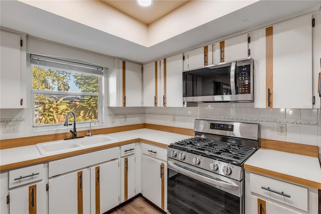 kitchen with appliances with stainless steel finishes, light wood-type flooring, backsplash, sink, and white cabinetry