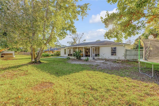 back of property with a sunroom, a trampoline, and a yard