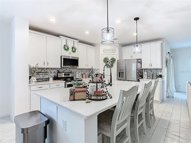 kitchen with white cabinets, appliances with stainless steel finishes, decorative light fixtures, and a center island with sink