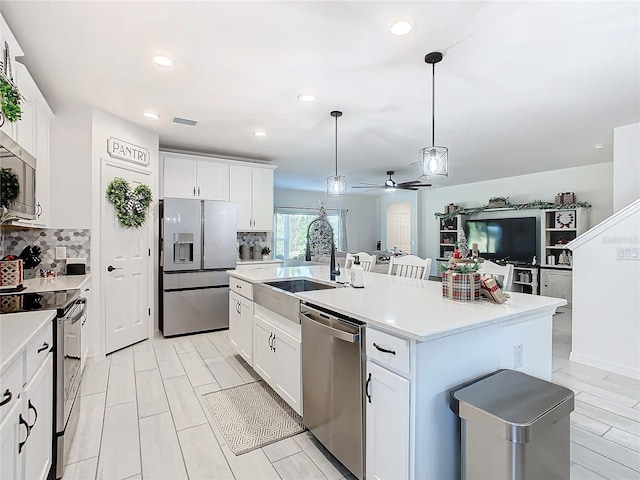 kitchen with white cabinets, pendant lighting, stainless steel appliances, and a kitchen island with sink