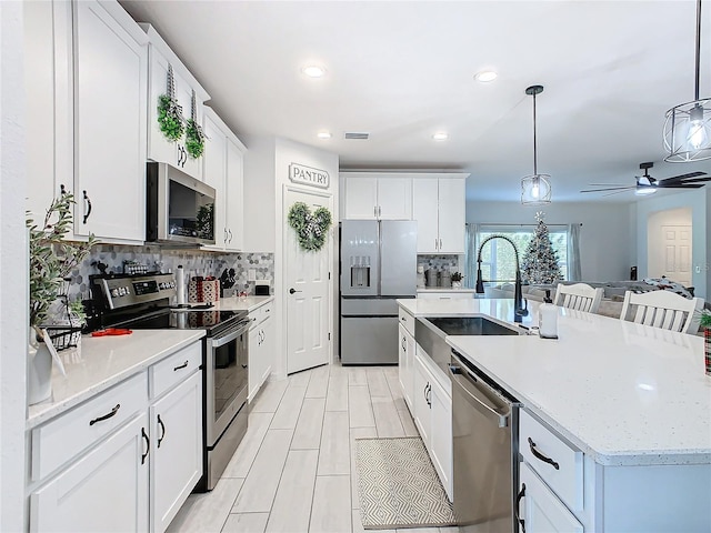 kitchen with ceiling fan, stainless steel appliances, pendant lighting, a center island with sink, and white cabinets