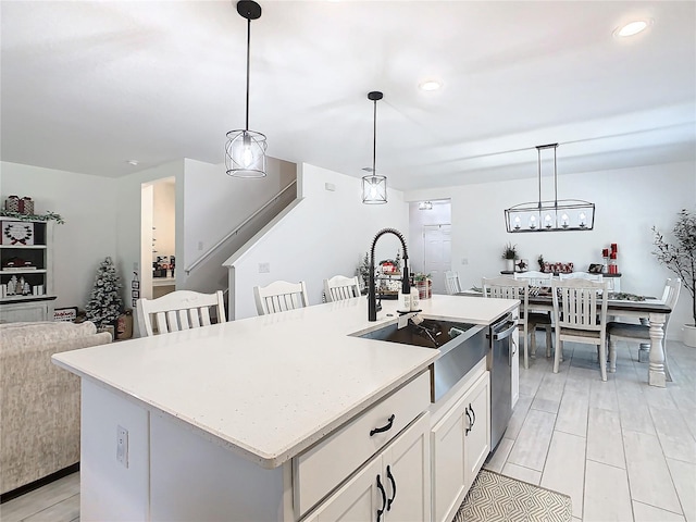 kitchen with sink, stainless steel dishwasher, decorative light fixtures, a center island with sink, and white cabinets