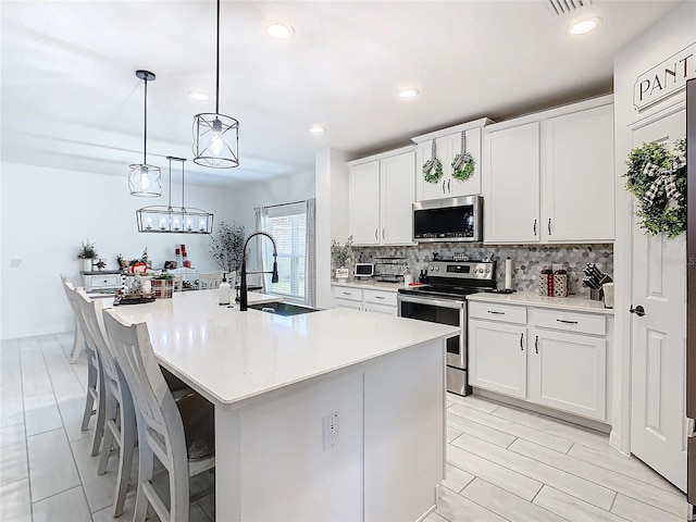 kitchen with white cabinetry, an island with sink, hanging light fixtures, and appliances with stainless steel finishes