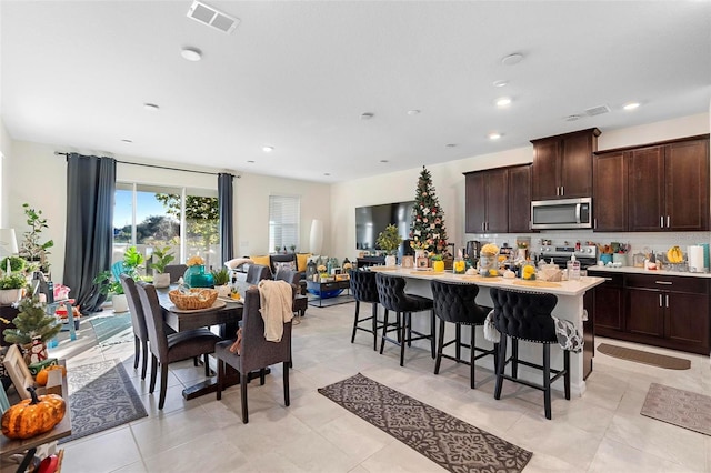 kitchen with a kitchen breakfast bar, a kitchen island with sink, dark brown cabinets, light tile patterned floors, and appliances with stainless steel finishes