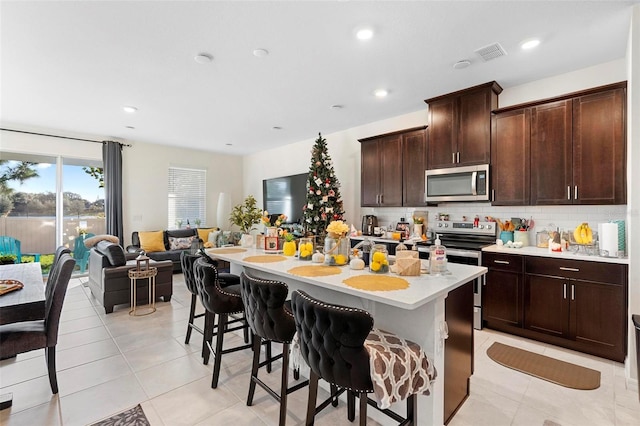 kitchen featuring a breakfast bar, a center island with sink, dark brown cabinets, and appliances with stainless steel finishes