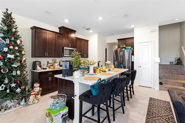 kitchen with appliances with stainless steel finishes, light tile patterned floors, a kitchen island with sink, and a kitchen breakfast bar