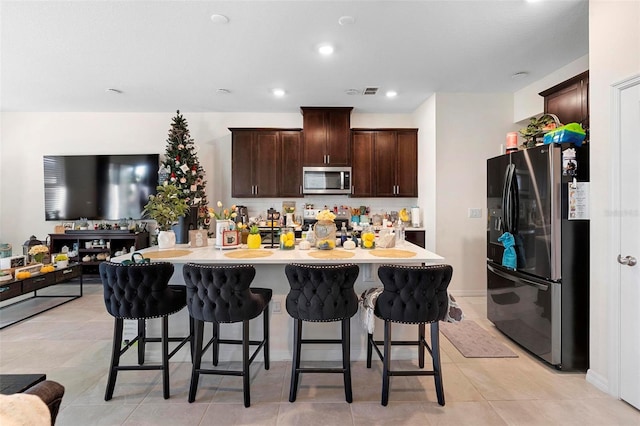 kitchen with a kitchen breakfast bar, kitchen peninsula, dark brown cabinets, light tile patterned flooring, and appliances with stainless steel finishes