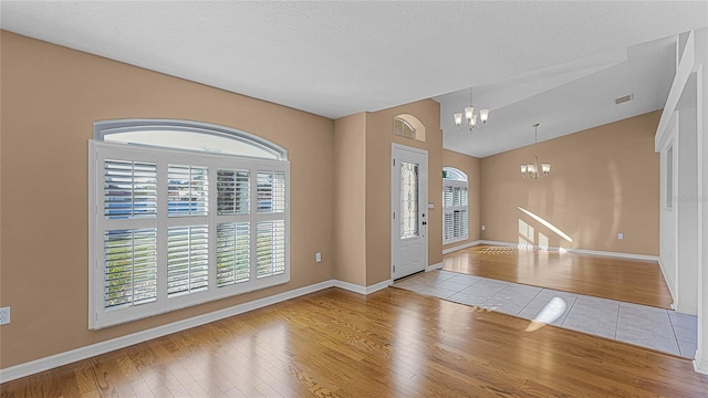 foyer with a textured ceiling, light wood-type flooring, lofted ceiling, and a notable chandelier