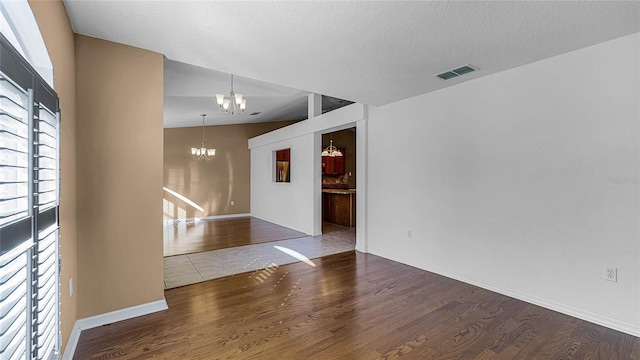 unfurnished room with a textured ceiling, wood-type flooring, lofted ceiling, and a notable chandelier