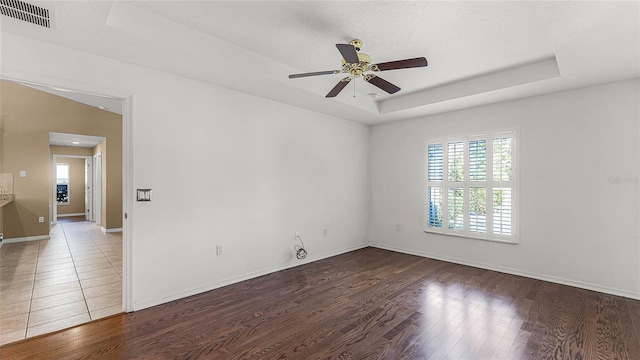 empty room with dark hardwood / wood-style floors, ceiling fan, and a tray ceiling