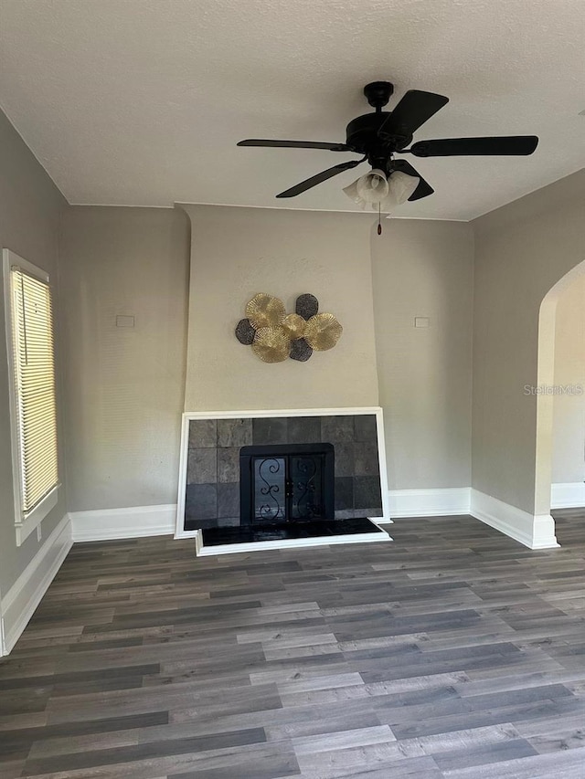 unfurnished living room with a textured ceiling, ceiling fan, dark wood-type flooring, and a tiled fireplace