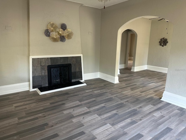 unfurnished living room featuring a tiled fireplace, ceiling fan, and dark hardwood / wood-style flooring