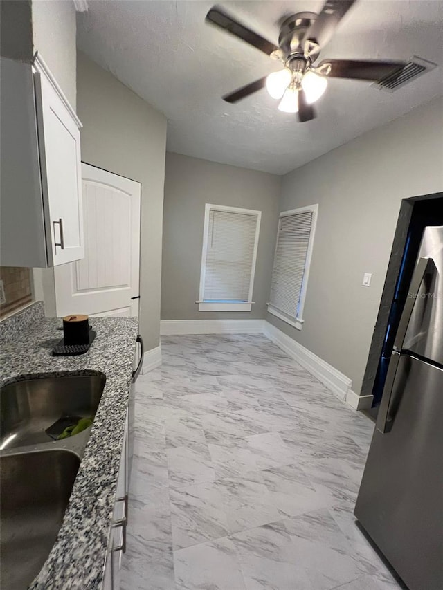 kitchen featuring sink, a textured ceiling, stone countertops, white cabinetry, and stainless steel refrigerator