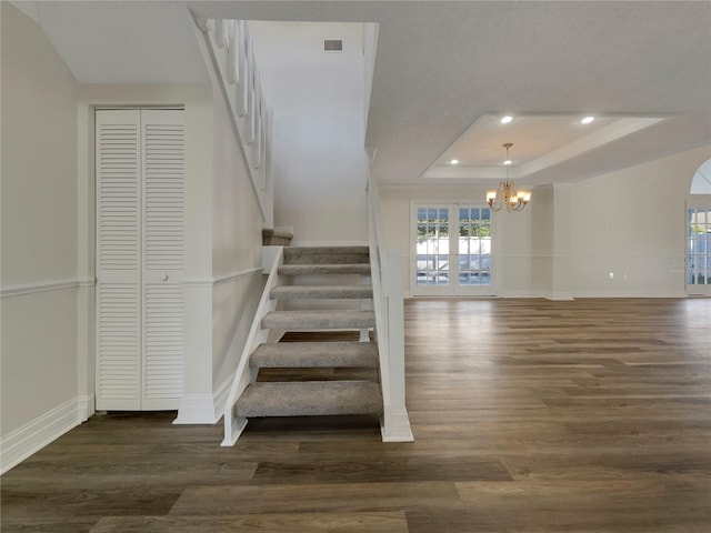 stairs with a raised ceiling, an inviting chandelier, and hardwood / wood-style flooring