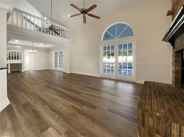 unfurnished living room featuring dark wood-type flooring, high vaulted ceiling, french doors, ceiling fan with notable chandelier, and a fireplace