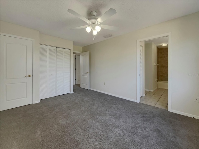 unfurnished bedroom featuring dark colored carpet, ceiling fan, ensuite bathroom, and a textured ceiling