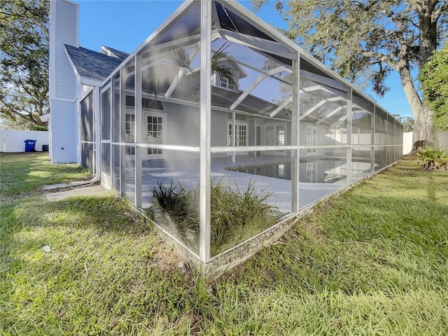 view of side of property with a lawn, glass enclosure, a patio area, and a swimming pool