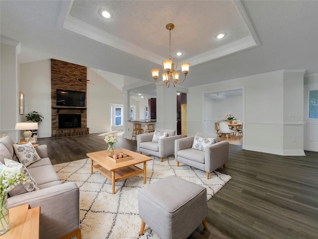 living room with an inviting chandelier, a raised ceiling, a brick fireplace, a textured ceiling, and wood-type flooring