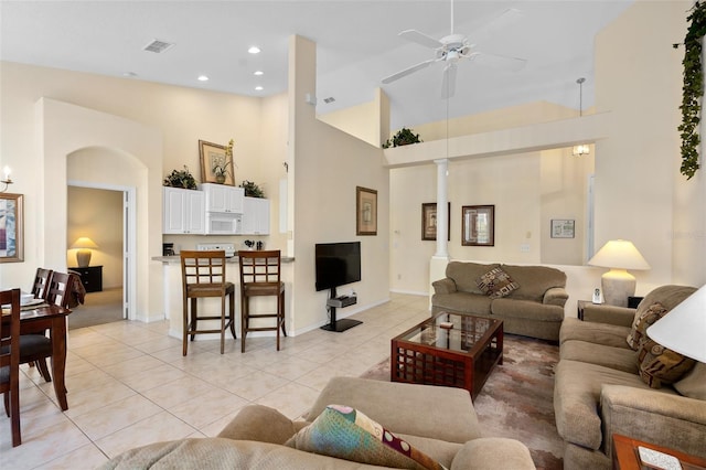 living room featuring decorative columns, ceiling fan, light tile patterned floors, and high vaulted ceiling