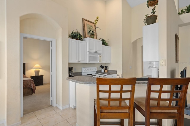 kitchen with kitchen peninsula, a kitchen bar, white appliances, white cabinetry, and light tile patterned flooring